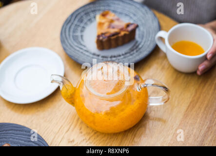 Orange Kaffee und Marmelade Kuchen auf Holz- Hintergrund. Stück pfirsich Gelee Kuchen aus ganze Torte Torte und einer Tasse Meer geschnitten - Sanddorn Tee. Frühstück im Stockfoto