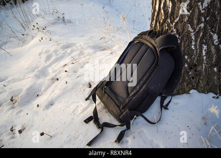 Schwarze Rucksack ist im Schnee, gemütliche schweren Rucksack, neben einem Baum Stockfoto