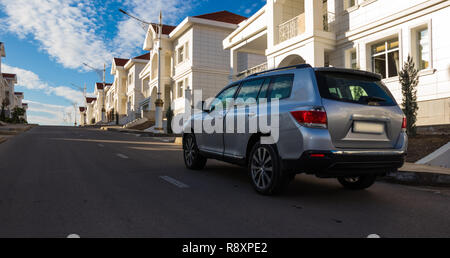 Ein silbernes Auto gegenüber weißen Villen mit einem roten Dach geparkt. Immobilien und Grundstücke, die in einer modernen Wohngegend Stockfoto