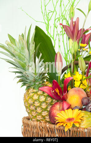 Weidenkorb voller Früchte und Blumen auf weißem Hintergrund Stockfoto