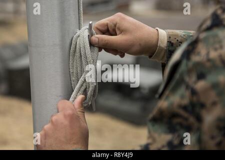 Ein US-Marine mit Sitz Batterie, 3.Bataillon, 12 Marines, bindet ein Seil an einem Fahnenmast während der Morgen Farben in der Hijudai Manöver, Japan, 6. März 2017. Marinesoldaten und Matrosen an der Artillerie relocation Training Programm rechtzeitige und genaue Brände zu stellen militärische beruflichen Spezialgebiet Fähigkeiten, Zug Marines/Matrosen in gemeinsamen Fähigkeiten zu erhalten, und professionelle militärische Ausbildung für das allgemeine Ziel der Verbesserung der Bekämpfung der Betriebsbereitschaft und internationale Beziehungen zu fördern. Stockfoto