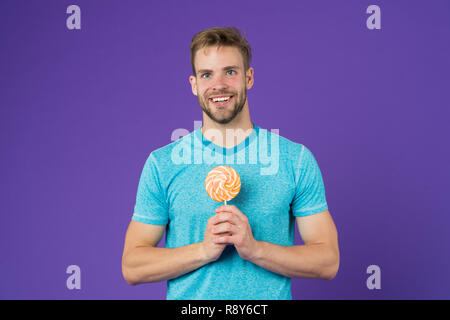 Zucker schädlich für die Gesundheit. Kerl halten Lollipop candy violett unterlegt. Mann schöner macho Essen großen bunten süßen Lutscher. Geschmack der Kindheit. Mann mit Borsten mag Lollipop. Cheat meal Konzept. Stockfoto