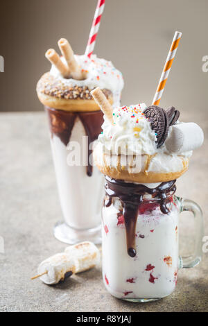 Milch Monster schüttelt oder Freak Schütteln. Big Crazy Milchshake oder Freakshake mit Leckereien und Süßigkeiten mischen. Süßes Getränk Dessert Sammlung in einem Gläser Stockfoto