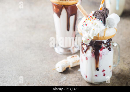 Milch Monster schüttelt oder Freak Schütteln. Big Crazy Milchshake oder Freakshake mit Leckereien und Süßigkeiten mischen. Süßes Getränk Dessert Sammlung in einem Gläser Stockfoto