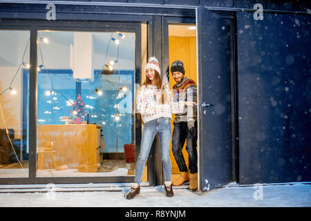 Junge glückliches Paar in Pullover feiern Winterurlaub vor einem wunderschönen eingerichteten Haus in den Bergen angezogen Stockfoto