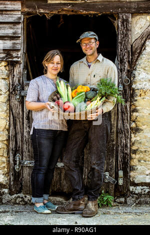 Lächelnd Bauer und Frau, die in der Scheune nebenan, Korb mit frisch geernteten Gemüse, an der Kamera schaut. Stockfoto