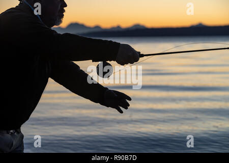 Die Silhouette eines Fliegenfischer Casting bei Sonnenaufgang für searun Küsten cutthroat Forelle an einem Strand an der Westküste der USA Stockfoto