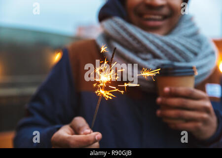 Zugeschnittenes Bild eines afrikanischen Jungen Mann posiert im Freien winter Konzept Kaffee trinken Holding bengal Lights. Stockfoto