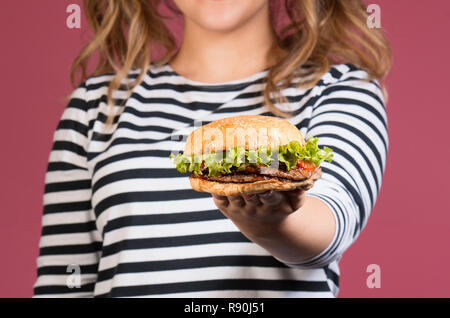 7/8-Foto von lächelnde Mädchen in gestreiften T-Shirt, Hamburger über bunte rosa Hintergrund. Schwerpunkt auf die Burger Stockfoto