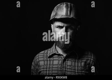 Builder oder Miner mit dicken Bart. Arbeiter mit brutalen Bild trägt Helm und Plaid Shirt. Mann mit strengen Gesichtsausdruck auf schwarzem Hintergrund isoliert, kopieren. Arbeits- und Schwerindustrie Konzept. Stockfoto