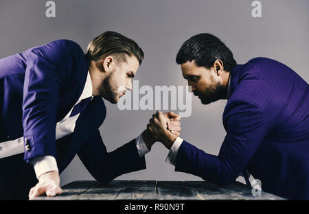 Taille-up Portrait von zwei verärgerte Geschäftsleute in Anzügen sitzen am Tisch und armwrestling auf dunklem Hintergrund, auf jedem anderen Suchen mit trotz Denken über einige Probleme, business Konflikt. Stockfoto