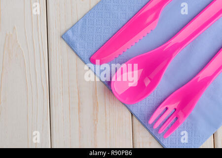 Rosa Besteck auf Violett serviette auf Holz- Hintergrund mit kopieren. Set aus bunten Kunststoff Gabel, Löffel und Messer. Stockfoto