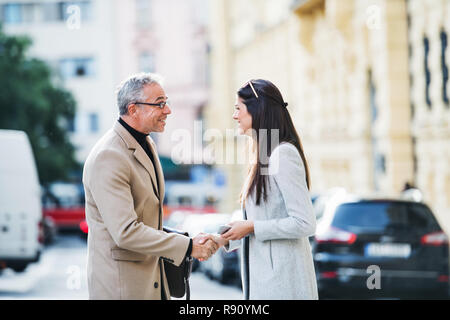Reifer Mann und junge Frau Geschäftspartner stehen draußen in der Stadt Prag, die Hände zu schütteln. Stockfoto