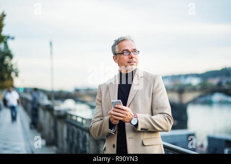 Reifen gut aussehender Geschäftsmann mit Smartphone steht die Moldau in Prag, die Stadt bei Sonnenuntergang, mit Smartphone. Stockfoto