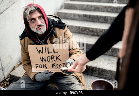 Eine nicht erkennbare Frau Geld geben für obdachlose Bettler Mann in der Stadt sitzen. Stockfoto