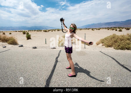 Junge Erwachsene weiblichen Fotografen auf einen Road Trip durch Death Valley National Park, steht auf und streckt ihre Arme und Beine Stockfoto