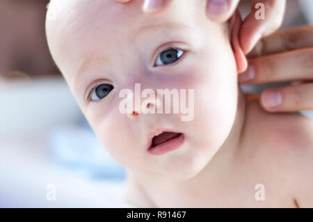 Junge Papa reinigt die Ohren der Baby mit einem Wattestäbchen. Das Konzept der Fürsorge für die Gesundheit des Kindes. Selektiver Fokus Stockfoto