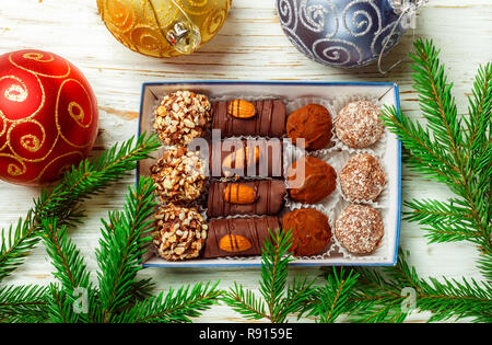 Satz von Pralinen. Trüffel mit Mandeln, Kokos und Cookie Krümel in einer Box auf einem alten weißen Tisch mit Tannenzweigen. Geschenk für Weihnachten und das neue Jahr. Stockfoto