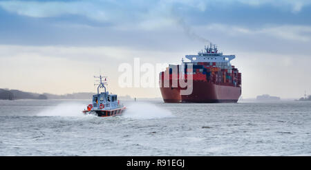 Ein kleines Lotsenboot vor einem riesigen Containerschiff auf der Elbe, Deutschland Stockfoto