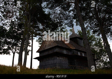 Alte hölzerne Kirche der Ukraine steht hoch in den Bergen von alten Bäumen umgeben Stockfoto