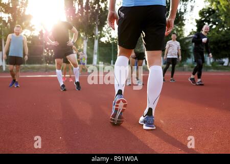 Zurück Bild eines Athleten in schwarzen Hosen und Turnschuhe. Männer warm up Outdoor auf dem Stadion. Sonnenstrahlen im Sommer warmen Tag. Freunde Zug zusammen Stockfoto