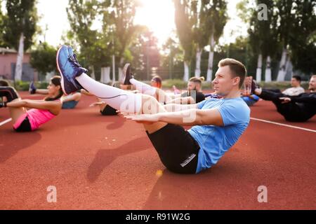 Die jungen Athleten in Sportbekleidung, Fitness Übungen. Menschen neben ihm wiederholen. Sonnig warmen Morgen. Gesunder Sport. Outdoor Training im Stadion Stockfoto