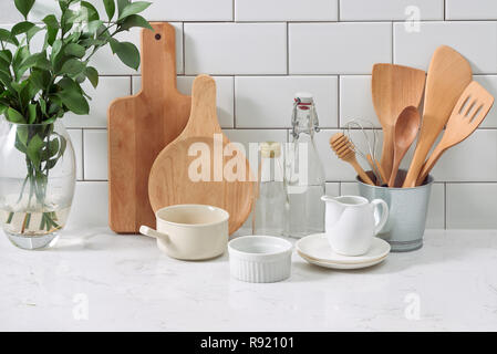 Einfache rustikale Küchenutensilien gegen weiße Holz Wand: grobe Keramik Topf mit Holz kochen Utensil, Stapel von keramischen Schalen, Kannen und Schalen aus Holz. Stockfoto