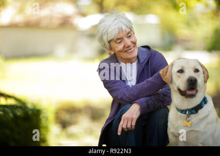 Lächelnd senior Frau streicheln Ihren Hund in ihrem Garten. Stockfoto
