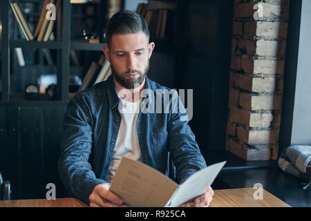 Junger Mann in einem Cafe sitzen am Tisch und beobachtete das Menü zu machen Stockfoto