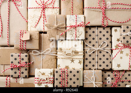 Weihnachten Hintergrund mit vielen dekorativen selbstgemachtes Geschenk Boxen in Braun Kraftpapier & rot weiß Garn umwickelt. Flach. Stockfoto