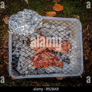 Leckere Steaks, gegrillt auf einem tragbaren & Einweg Grill Stockfoto