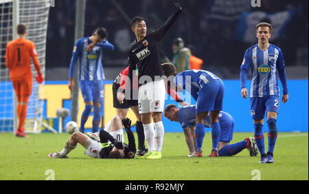 18. Dezember 2018, Berlin: Fussball: 1. Fussballbundesliga, 16. Spieltag, Hertha BSC - FC Augsburg im Olympiastadion. Der Augsburger Daniel Baier (l) ist am Boden verletzt, Ondrej Duda (hinten, 2. von rechts) von Hertha BSC kniet auf dem Gras mit einem Schmerz verzerrte Gesicht. Der Augsburger Dong-won Ji (vorne, Mitte) ruft die Sanitäter. Foto: Andreas Gora/dpa - WICHTIGER HINWEIS: In Übereinstimmung mit den Anforderungen der DFL Deutsche Fußball Liga oder der DFB Deutscher Fußball-Bund ist es untersagt, zu verwenden oder verwendet Fotos im Stadion und/oder das Spiel in Form von Bildern und/oder Videos getroffen haben Stockfoto