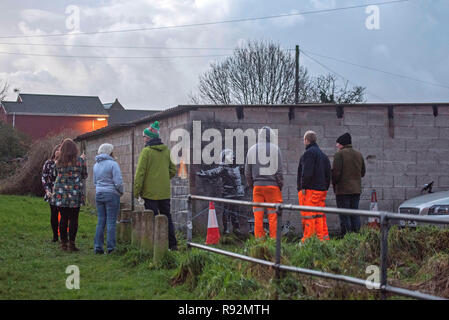 Port Talbot, Wales, UK. 19. Dezember, 2018. Die Einwohner von Taibach in Port Talbot prüfen Graffiti, die über Nacht auf eine Garage, die sich durch die anonyme Street Artist Banksy erschienen. Das Kunstwerk zeigt ein Kind mit offenen Armen spielen in, was scheint, Schnee mit dem Schlitten an seiner Seite zu sein, aber die andere Seite der Mauer zeigt, ist die Asche aus einem Mülleimer in Brand. Credit: Phil Rees/Alamy leben Nachrichten Stockfoto