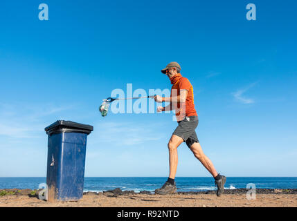 Ein Plogger/Jogger sammelt Plastikmüll am Strand während seines morgendlichen Lauf Stockfoto