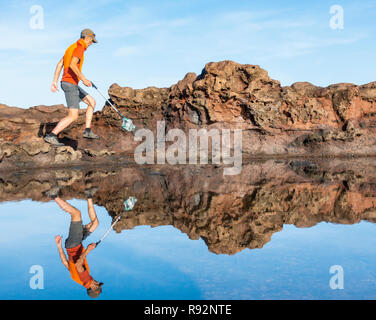 Ein Plogger/Jogger sammelt Plastikmüll am Strand während seines morgendlichen Lauf Stockfoto