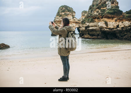 Mädchen mit einem Rucksack Touristen fotografieren eine schöne Landschaft an der Atlantikküste. Stockfoto