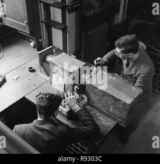 1950, Universität Oxford, Ansicht von oben von zwei männlichen Wissenschaft Studenten Experimente Messung der Spannung mit Meter und speziell angefertigten Schläuche und Holzbox. Im Bild zu sehen ist ein Schild mit der Aufschrift "Gefahr 60.000 Volt' Stockfoto