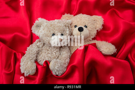 Liebe, Valentines Tag Konzept, festen Umarmung. Zwei Teddybären, die als Paar im Bett, Rot Satin Hintergrund Stockfoto