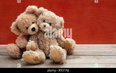 Liebe, Freundschaft, Konzept, festen Umarmung. Zwei Teddybären, die als Paar auf Holzboden, rote Wand Hintergrund, kopieren. Stockfoto