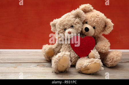 Liebe, Freundschaft, Konzept, festen Umarmung. Zwei Teddybären, die als Paar auf Holzboden, rote Wand Hintergrund, kopieren. Stockfoto