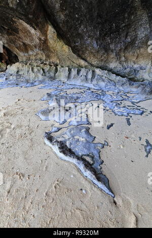 Sehr karstige Relief der Kalkfelsen mit Geschwärzter-weißlich-rötlich-bläuliche Felsen erodiert. Eingang Loch zur Cudugnon Höhle - nasser Sand der Beac Stockfoto