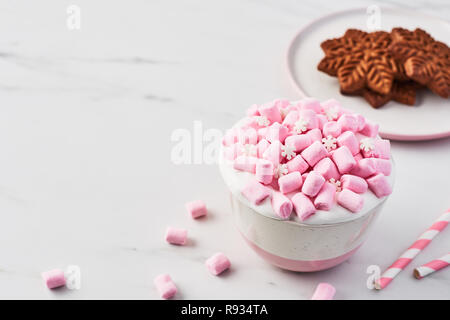 Heiße Schokolade oder Kakao mit Schlagsahne und pink Marshmallow candy in rosa und weiße Tasse mit Weihnachten Lebkuchen Cookie auf weißem Marmor tisch. Co Stockfoto