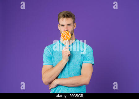 Mann mit Borsten mag Lollipop. Cheat meal Konzept. Zucker schädlich für die Gesundheit. Kerl halten Lollipop candy violett unterlegt. Mann schöner macho Essen großen bunten süßen Lutscher. Geschmack der Kindheit. Stockfoto