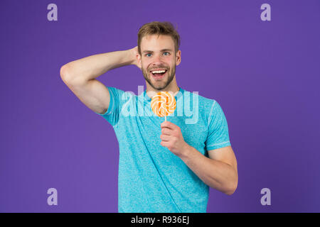 Mann schöner macho Essen großen bunten süßen Lutscher. Geschmack der Kindheit. Man bärtige Erwachsene mag Lollipop. Sweet Tooth Konzept. Zucker schädlich für die Gesundheit. Kerl halten Lollipop candy violett unterlegt. Stockfoto