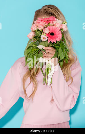 Frau in rosa Kleidung versteckt sich hinter schönen Blumenstrauß auf blauem Hintergrund Stockfoto