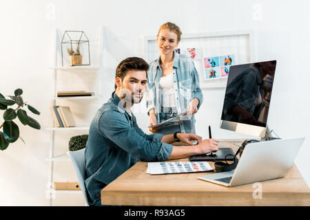 Junge Fotografen lächeln auf die Kamera beim Retuschieren von Fotos im Büro Stockfoto
