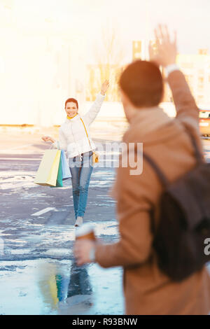 Attraktives Mädchen mit Tüten Winken mit der Hand auf dem Parkplatz zu Freund Stockfoto