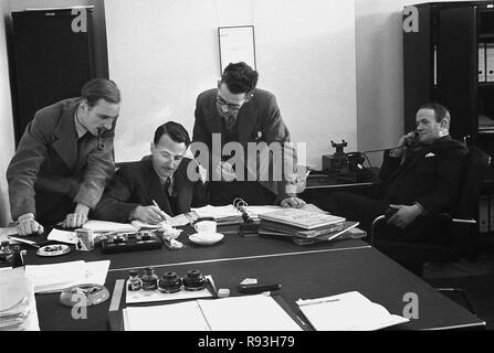 1940 s, Unternehmensleiter einer synthetischen Seidenfabrik in einem Büro, mit einem Mann am Schreibtisch ein Gespräch am Telefon und die anderen drei Führungskräfte, die an papework in einer Datei auf einem Schreibtisch sitzen, mit einem Rauchen einer Pfeife, South Wales, UK. Stockfoto