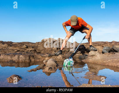 Ein Plogger/Jogger sammelt Plastikmüll am Strand während seines morgendlichen Lauf Stockfoto