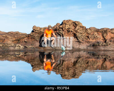 Ein Plogger/Jogger sammelt Plastikmüll am Strand während seines morgendlichen Lauf Stockfoto